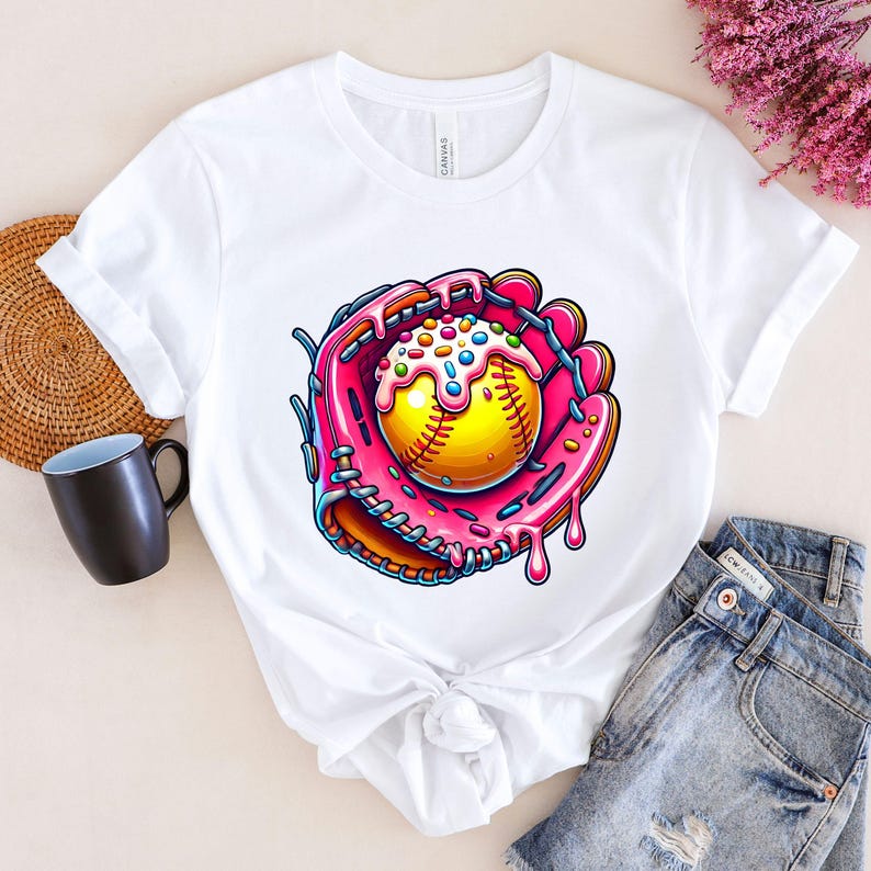 May include: White t-shirt with a graphic of a pink and yellow softball in a pink and white baseball glove with sprinkles on top. The glove is dripping pink icing.
