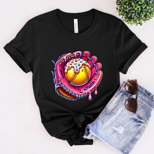May include: Black t-shirt with a graphic of a pink and white softball in a pink and white catcher's mitt. The softball is covered in sprinkles.