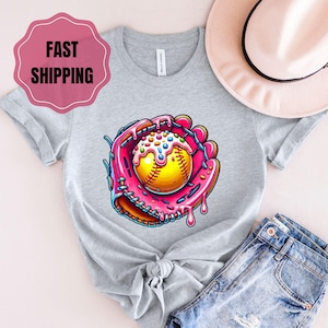 May include: A gray t-shirt with a pink and yellow graphic of a baseball in a catcher's mitt with pink frosting and sprinkles. The graphic is in the center of the shirt.