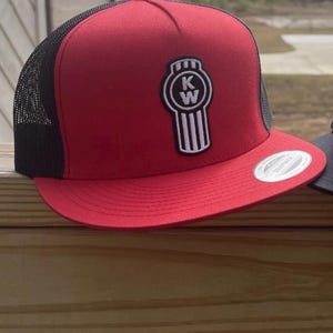 May include: A red and black trucker hat with a white "KW" logo on the front. The logo is a stylised image of a truck grill.