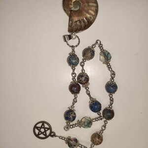 May include: A silver chain with a brown and iridescent ammonite pendant, brown and blue speckled beads, clear crystal beads, and a silver pentagram charm.