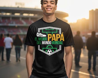 Può includere: T-shirt nero con grafica a tema calcistico. Il design include un contorno di campo da calcio, una scarpa da calcio, un pallone da calcio e il testo spagnolo "EL MEJOR PAPÁ DEL MUNDO MUNDIAL" in bianco e giallo. La maglietta è indossata da una persona.