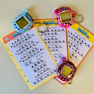May include: A collection of vintage Tamagotchi digital pets in blue, pink, and red, with keychains, alongside yellow cards featuring character family charts. The cards include text such as "Smart Family" and "Sociable Family".