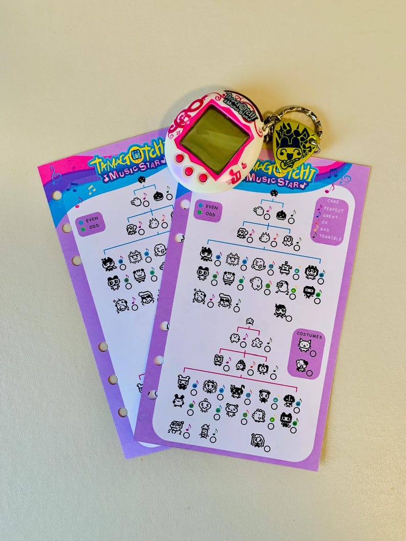 May include: A white and pink Tamagotchi Music Star digital pet with a keychain and two purple evolution charts. The charts feature character illustrations and the text "Tamagotchi Music Star".
