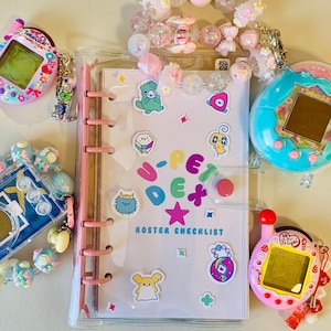 May include: A clear binder with a pink spine and a "U-PET" roster checklist. The binder is surrounded by colorful stickers, beaded bracelets, and several Tamagotchi virtual pet devices in pink, blue, and teal.