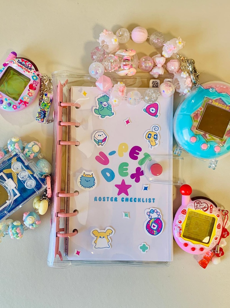 May include: A clear binder with a pink spine and a "U-PET" roster checklist. The binder is surrounded by colorful stickers, beaded bracelets, and several Tamagotchi virtual pet devices in pink, blue, and teal.