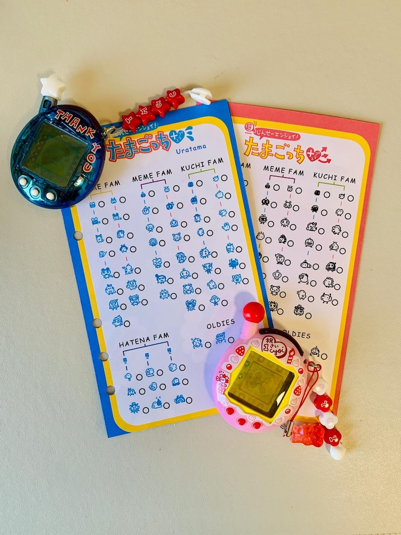 May include: Two Tamagotchi virtual pet devices, one blue and one pink, with matching charts. The blue device has the text "THANK YOU" and the pink device has a red button. The charts have Japanese text and illustrations of characters.