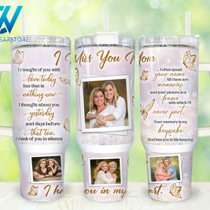 May include: A white tumbler with a pink background and gold glitter. The tumbler has a white handle and a straw. The tumbler has a picture of two women and the text "I Miss You Mom" on the front. The text "I often speak your name. All I have are memories and your picture in a frame with which I'll never part. Your memory is my keepsake. God has you in his keeping." is on the back of the tumbler.