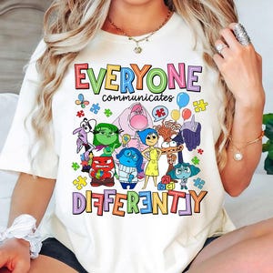 Pu&ograve; includere: Maglietta bianca con una grafica colorata di personaggi del film Inside Out. Il testo "Tutti comunicano in modo diverso" &egrave; stampato sulla maglietta.