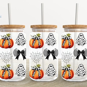 Op de afbeelding: Drie glazen bekers met houten deksels en metalen rietjes. Elke beker heeft een Halloween-thema met pompoenen, geesten, strikken en spinnenwebben in zwart, wit en oranje.