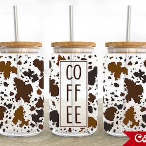 May include: Three glass coffee tumblers with wooden lids and metal straws. The tumblers feature a cow print design in brown and white. The center tumbler has the word "COFFEE" in a rectangular frame.