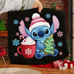 Könnte beinhalten: Schwarze Decke mit einer blauen Cartoonfigur, die einen Weihnachtsmannhut trägt und einen Weihnachtsbaum hält. Eine rote Tasse mit Schlagsahne und Schneeflocken befindet sich links. Schneeflocken sind um das Design verstreut.