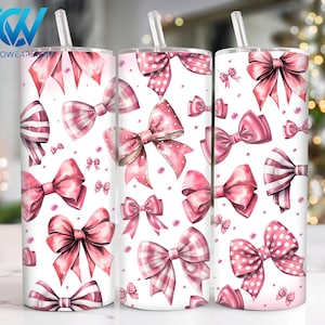 May include: Three pink and white stainless steel tumblers with a pattern of pink bows on a white background. The tumblers have lids and straws.