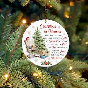 Puede incluir: Adorno navideño redondo blanco con una ilustración de acuarela de una mecedora, un árbol de Navidad y regalos. El adorno tiene el texto "Navidad en el cielo" y un poema sobre seres queridos que han fallecido.