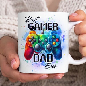 Op de afbeelding: Witte keramische mok met een kleurrijk aquarelontwerp van een videogamecontroller. De tekst "Best Gamer Dad Ever" staat op de mok gedrukt.