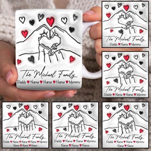 Puede incluir: Taza de cerámica blanca con un contorno negro de dos manos formando un corazón con un corazón más pequeño en su interior. El texto "The Michael Family" está impreso debajo de la imagen con las palabras "Daddy", "Name", "Mommy" y corazones entre las palabras.