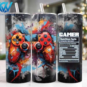 Può includere: Un bicchiere a tema gamer con un design astratto colorato che presenta un controller per videogiochi. Il bicchiere ha uno sfondo nero con schizzi di vernice rossa, blu, gialla e arancione. Il testo "GAMER Nutrition Facts" è stampato sul lato destro del bicchiere con un elenco di "Nutrition Facts" per i giocatori.