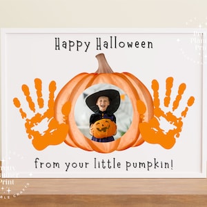 Op de afbeelding: Een wit frame met een witte achtergrond en een pompoen met een kinderfoto erin. De pompoen wordt omringd door twee oranje handafdrukken. De tekst "Happy Halloween van je kleine pompoen!" staat onder de pompoen.