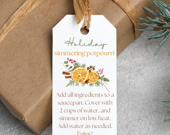 May include: A white gift tag with a green and orange illustration of a holiday simmering potpourri recipe. The text on the tag reads "Holiday simmering potpourri" and includes instructions for making the potpourri. Add all ingredients to a saucepan. Cover with 2 cups of water, and simmer on low heat. Add water as needed. Enjoy!