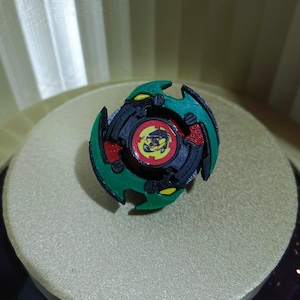 May include: A green, black, and red spinning top with a yellow and black dragon design. The top is a popular toy for children and adults.