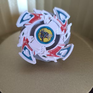 May include: White, red, and blue plastic Beyblade with a dragon design and the text "DRAGON GT" on the side. The Beyblade has a clear plastic center with a yellow and blue dragon design and the text "DRAGON GT" on the side.