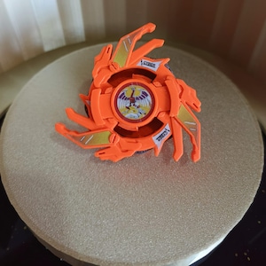 May include: Orange and gold plastic toy with a red and white circular design in the center. The toy has the word "CYBER" printed on it.