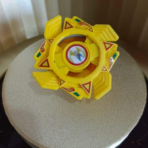 May include: A yellow plastic toy top with a red, white, and blue design in the center. The top has a star-shaped design with green and red accents.