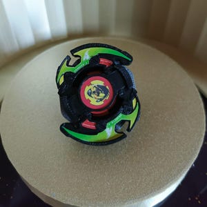 May include: Black and green spinning top toy with a red and yellow center featuring a dragon design. The top has the words "Draciel" and "Balance" printed on it.