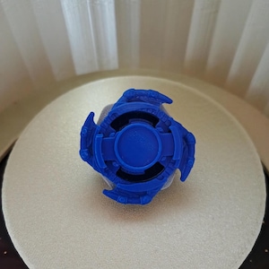 May include: A blue plastic toy with a circular center and three arms with teeth. The toy is designed to spin.