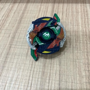 May include: A blue, green, red, and yellow spinning top with a silver rim. The top has a dragon design and the text "Draizer" on it.