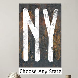 May include: A rectangular wall art piece featuring the letters "NY" in white against a dark, textured background. The artwork hangs above a small table with a sculpture and a book. The text "Choose Any State" is below the artwork.