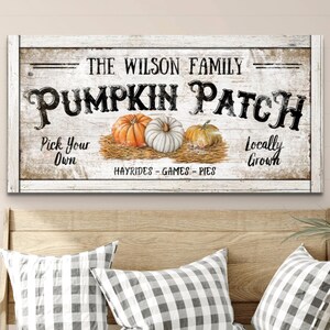 May include: A white wooden sign with black text that reads "The Wilson Family Pumpkin Patch". The sign has a rustic look and features a hay bale with three pumpkins on top. The text also reads "Pick Your Own", "Locally Grown", and "Hayrides - Games - Pies".