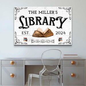 May include: White wooden sign with black text that reads "The Miller's Library Est. 2024 Get a Better Read on the World". The sign features a decorative floral design and an illustration of an open book.