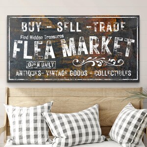 May include: A rustic, weathered sign with the text "BUY - SELL - TRADE" and "FLEA MARKET" in white lettering. The sign also includes the text "Find Hidden Treasures", "OPEN DAILY", "ANTIQUES - VINTAGE GOODS - COLLECTIBLES".