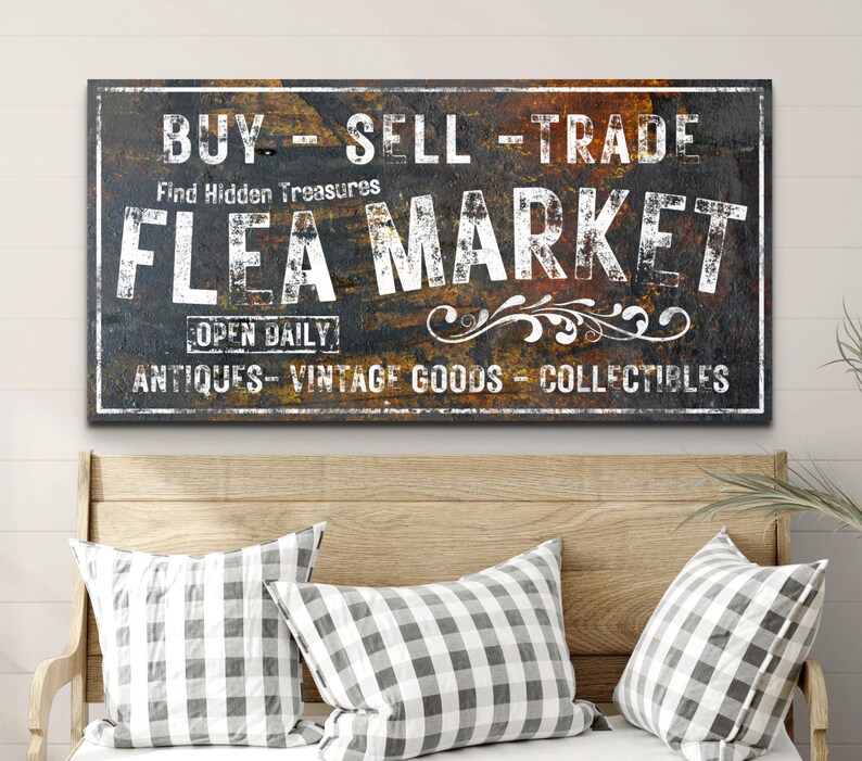 May include: A rustic, weathered sign with the text "BUY - SELL - TRADE" and "FLEA MARKET" in white lettering. The sign also includes the text "Find Hidden Treasures", "OPEN DAILY", "ANTIQUES - VINTAGE GOODS - COLLECTIBLES".