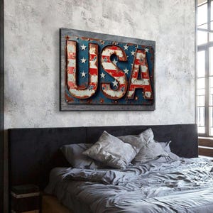 May include: A distressed metal sign with the word "USA" in large, bold letters. The letters are painted in red, white, and blue, resembling the American flag. The sign is hanging on a gray wall above a bed with gray bedding.