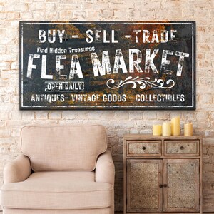 May include: A vintage-style sign with a rusty metal background and white lettering that reads "BUY - SELL - TRADE Find Hidden Treasures FLEA MARKET OPEN DAILY ANTIQUES - VINTAGE GOODS - COLLECTIBLES".