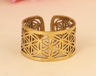 Könnte beinhalten: Ein goldfarbener offener Manschettenring mit einem geometrischen Blumenmuster. Der Ring aus Metall hat ein offenes Design, das eine verstellbare Passform ermöglicht. Der Ring wird auf einer hellbeigen Oberfläche mit einer rosa Rose im Hintergrund präsentiert.
