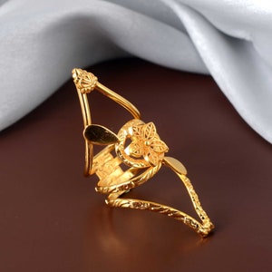 Puede incluir: Un anillo de tono dorado con un diseño floral. El anillo está hecho de metal y tiene un diseño delicado e intrincado.