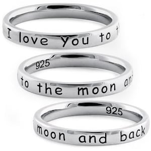 May include: Three silver-colored metal rings stacked vertically. Each ring features black engraved text. The top ring reads I love you to, the middle ring reads to the moon and, and the bottom ring reads moon and back. The middle and bottom rings show 925.