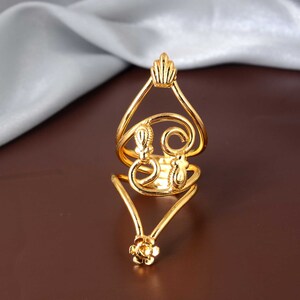 Puede incluir: Un anillo de tono dorado con un diseño delicado e intrincado. El anillo presenta una banda doble con un motivo floral en la base y un diseño de espiral en la parte superior.