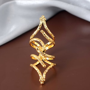 Puede incluir: Un anillo de tono dorado con un diseño geométrico. El anillo está hecho de múltiples bandas entrelazadas con una superficie texturizada.