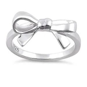 May include: A polished silver-tone ring featuring a prominent bow design on the top. The band is smooth and circular, with the hallmark 925 clearly engraved on the inner surface, indicating the metal composition of this jewelry piece.