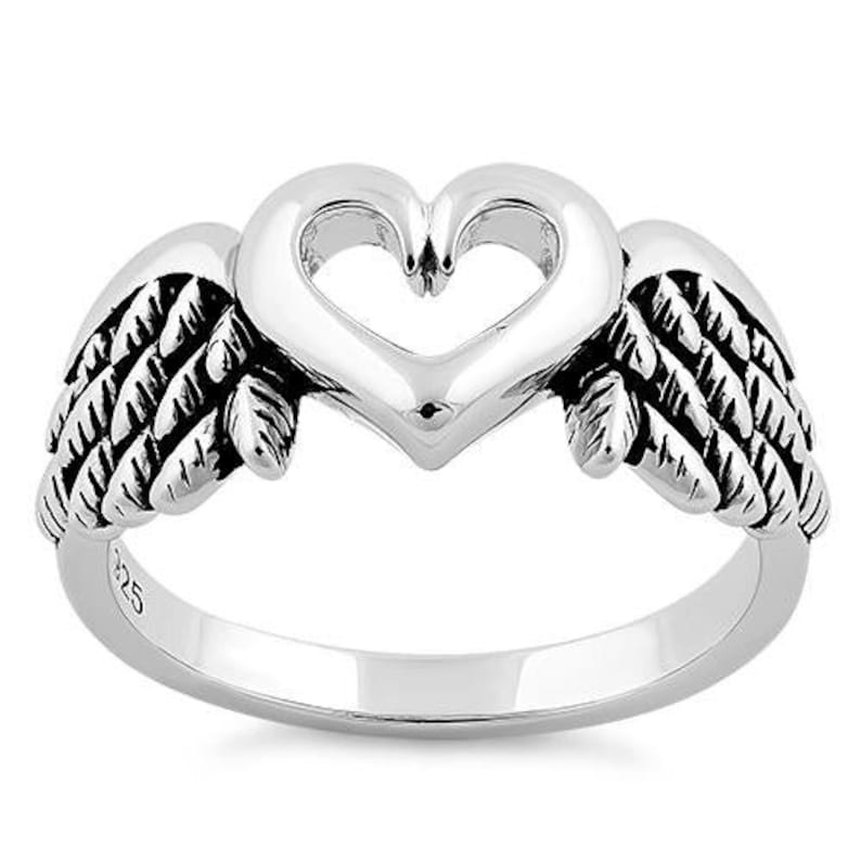 May include: A silver ring featuring a heart-shaped design with open space in the center, flanked by detailed wing accents. The ring is made of polished metal, showcasing a bright, reflective surface. The ring is a piece of jewelry.