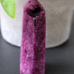 May include: A deep purple crystal point with a natural hole in the centre. The crystal has a rough, textured surface.