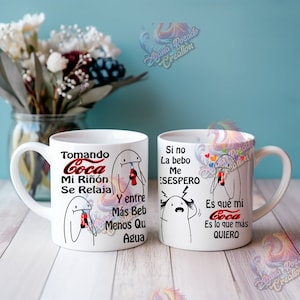 May include: Two white ceramic mugs with black and red illustrations. The text on the mugs reads "Tomando Coca Mi Riñón Se Relaja Y entre Más Beb Menos Qu Agua" and "Si no La bebo Me ESESPERO Es que mi Coca Es lo que más QUIERO".