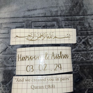 May include: A white card with gold lettering that says "Haroon & Aisha 03.02.24" and "And we created you in pairs" Quran (78:8).