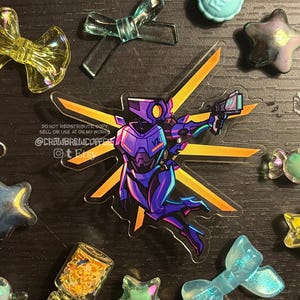 Op de afbeelding: Een doorzichtige acryl hanger met een paarse en blauwe robotfiguur met gele vleugelachtige accenten, die een klein handvuurwapen vasthoudt. Het ontwerp bevat de tekst DO NOT REDISTRIBUTE, COPY, SELL, OR USE AI ON MY WORKS @CROWBREWCOFFEE.