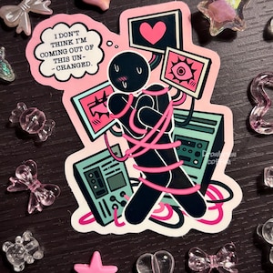 May include: A sticker featuring a black figure wrapped in pink cords, surrounded by computer screens with hearts and eyes. The sticker has the text "I don't think I'm coming out of this un-changed." Scattered around are pink and clear decorative embellishments.