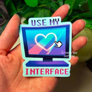 May include: A die-cut sticker shaped like a computer monitor with a blue and purple frame. The screen displays a glowing white heart icon and a pixelated mouse cursor. The text "USE MY" appears above the screen and "INTERFACE" below it.